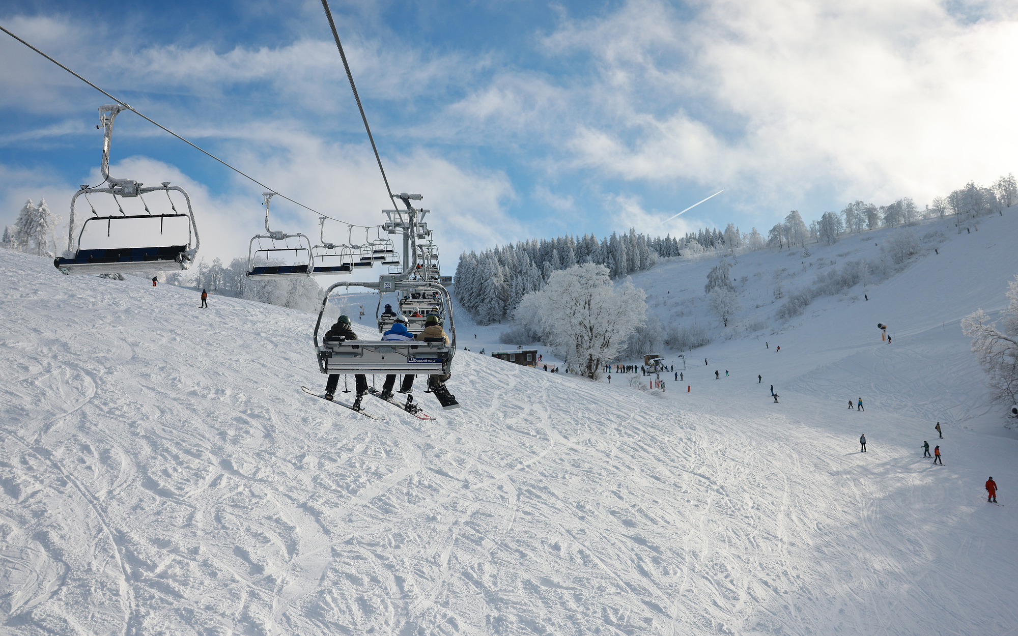 Ein Foto aus einem Sessellift heraus auf einen Skihang mit Ski- und Snowboardfahrern.