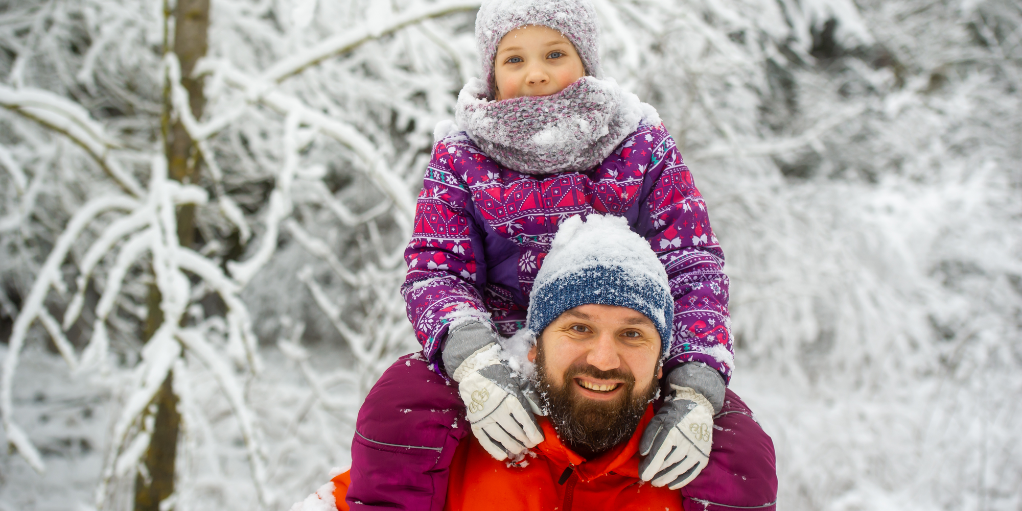 Ein Vater läuft mit seinem Kind auf Huckepack durch den Winterwald.