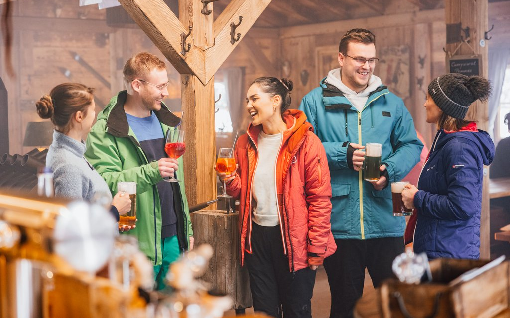 Eine Gruppe Freunde, die mit Getränken in einer Hütte steht und sich unterhält und lacht.