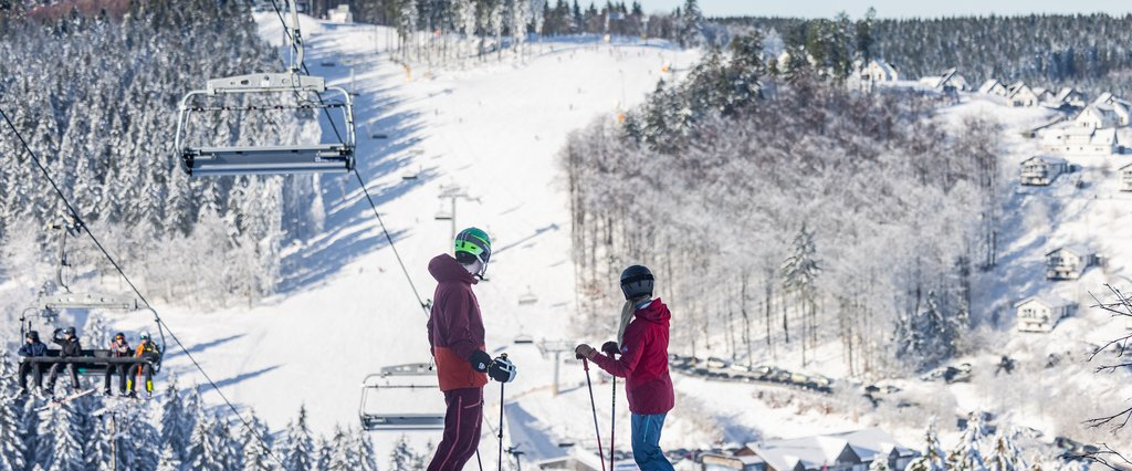 Zwei Skifahrer stehen oben am Skihang und blicken Richtung Tal.