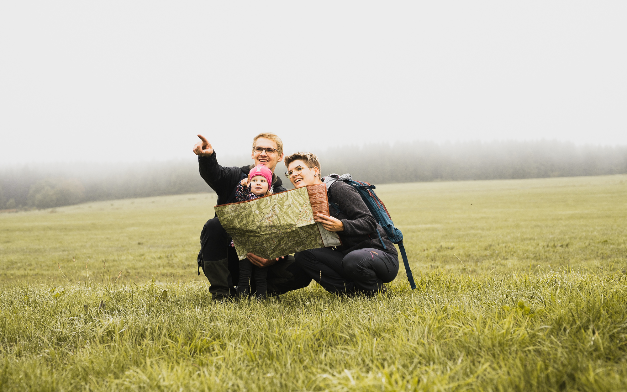 Familie hockt mit Kleinkind und Wanderkarte auf einer Wiese und plant die nächste Wandertour.