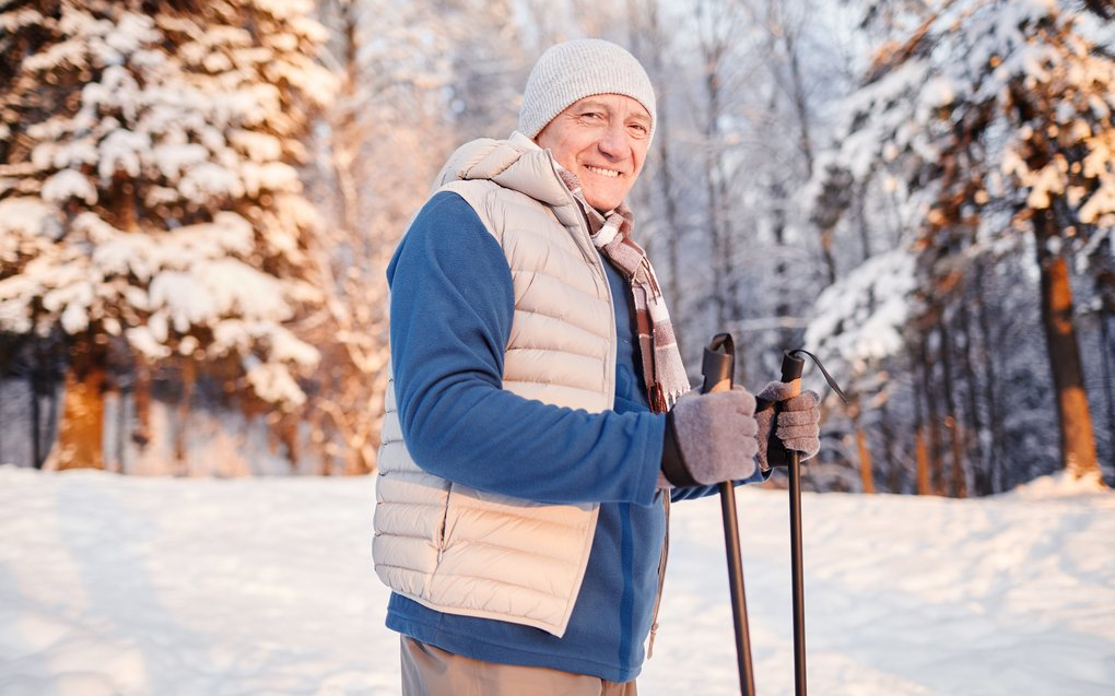 Ein Mann mit Wanderstöcken zum winterwandern lächelt in die Kamera.