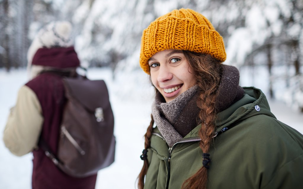 Zwei Frauen im schneebedeckten Wald, die eine lächelt in die Kamera.