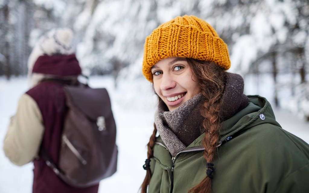 Zwei Frauen im schneebedeckten Wald, die eine lächelt in die Kamera.