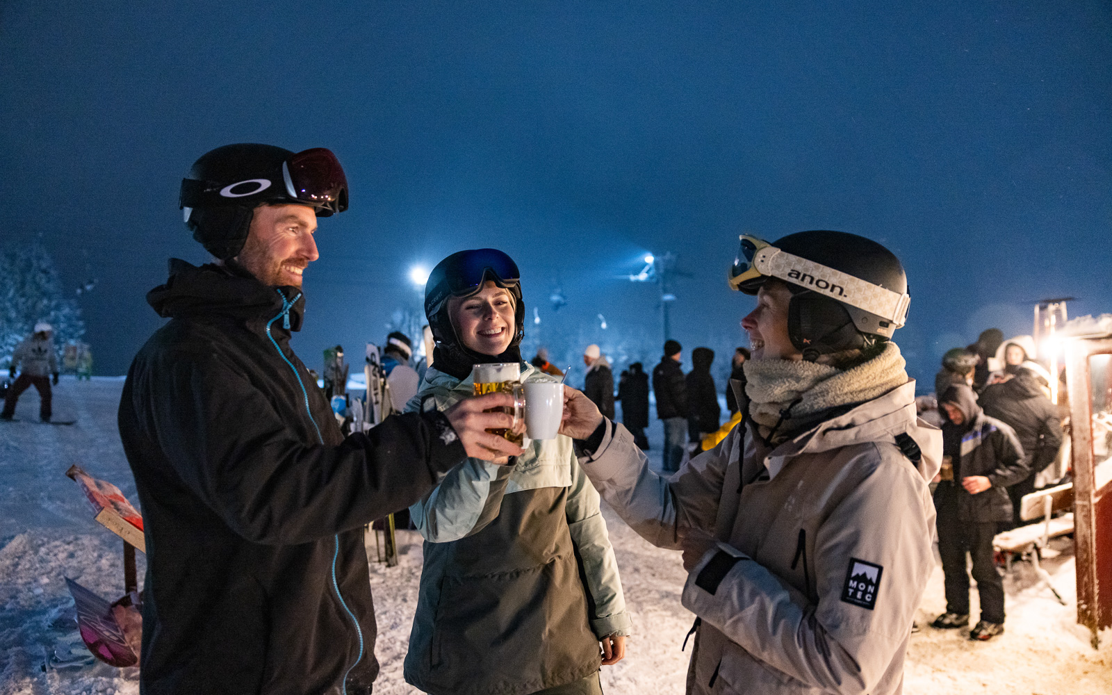 Skifahrer prosten sich beim Skifahren unter Flutlicht mit Kakao zu