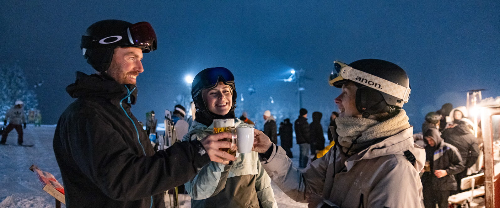 Skifahrer prosten sich beim Skifahren unter Flutlicht mit Kakao zu