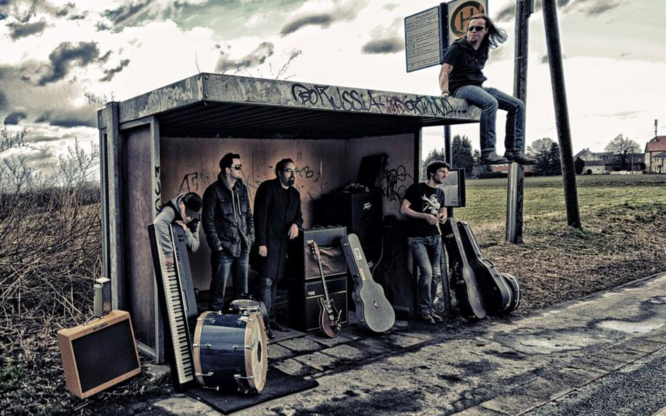 Die Band Rockaholix posieren mit ihren Instrumenten an einer Bushaltestelle.