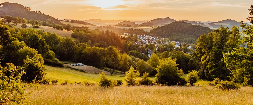 Eine Landschaft aus Wiesen und Wäldern mit ein paar Häusern und Blick auf einen der Trekkingplätze zum zelten in der untergehenden Abendsonne.