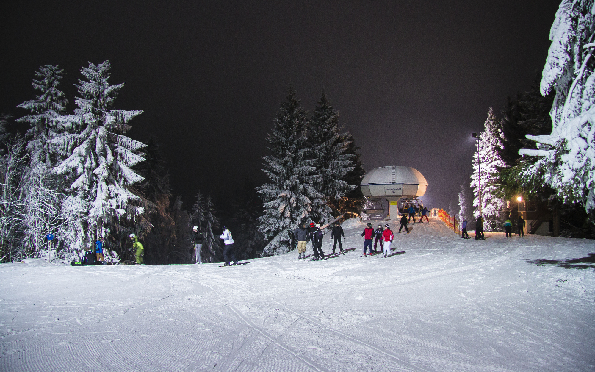 Ein paar Skifahrer an der Bergstation des Skilifts bei Flutlicht.