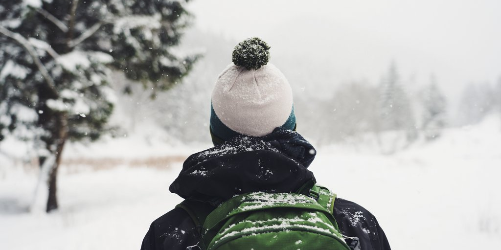 Eine Person mit Mütze und Rucksack wandert durch eine schneebedeckte Landschaft.