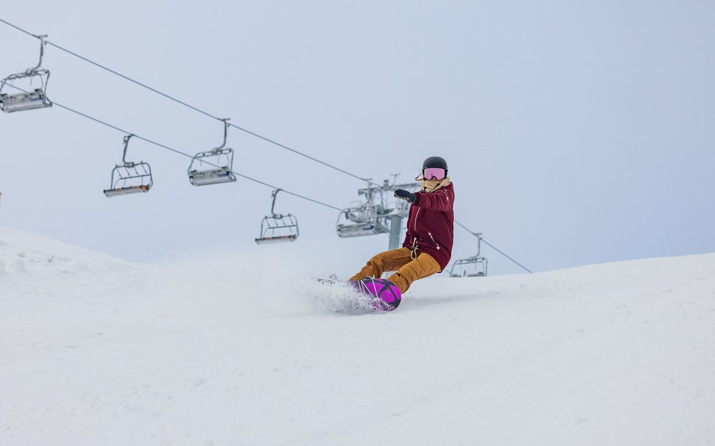 Ein Snowboardfahrer fährt auf seinem Snowboard einen Skihang hinunter.