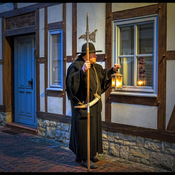 Ein Mann im historischen Nachtwächtergewand steht vor einem Fachwerkhaus.