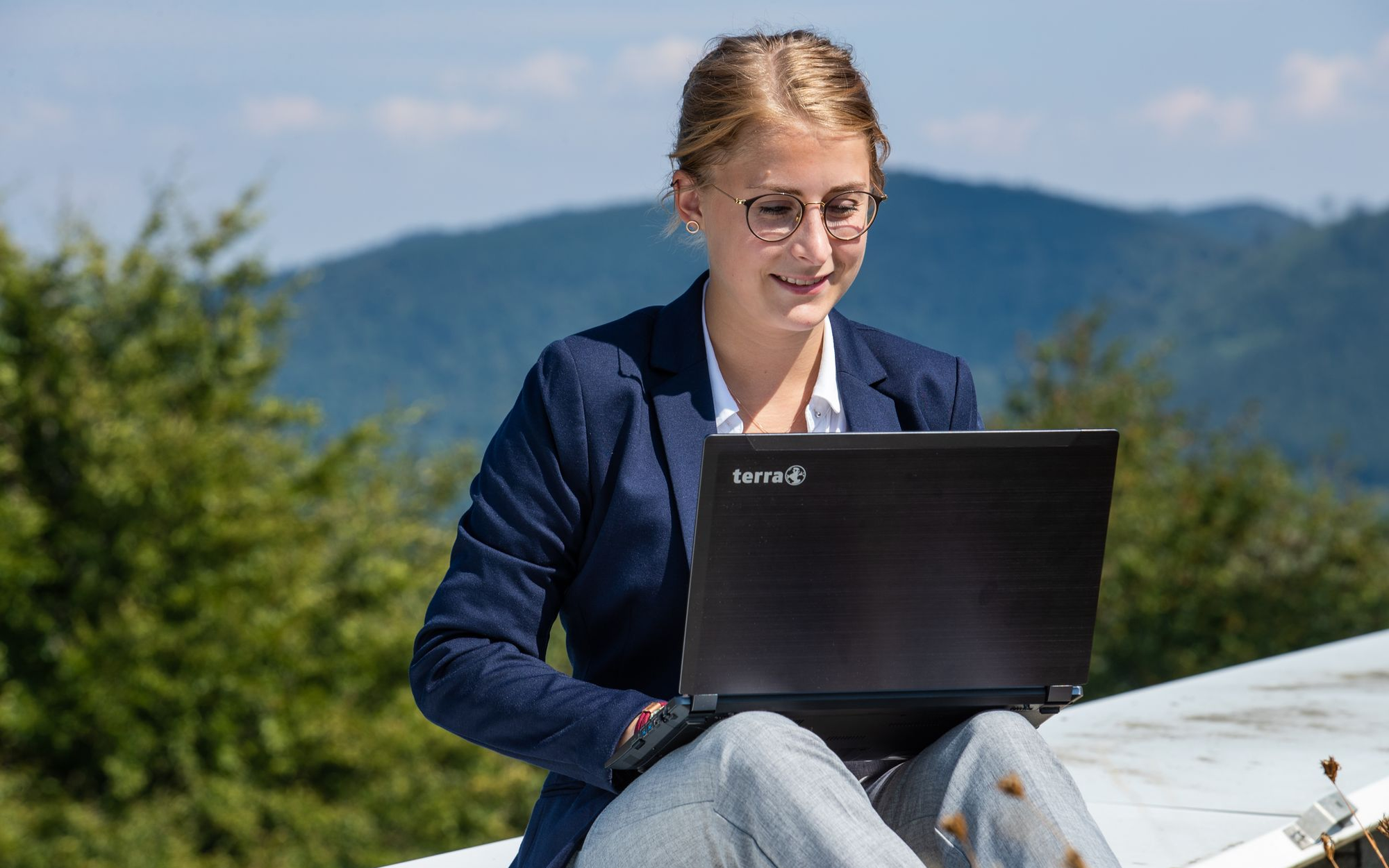 Eine Frau sitzt mit ihrem Laptop auf den Knien im Freien und arbeitet.