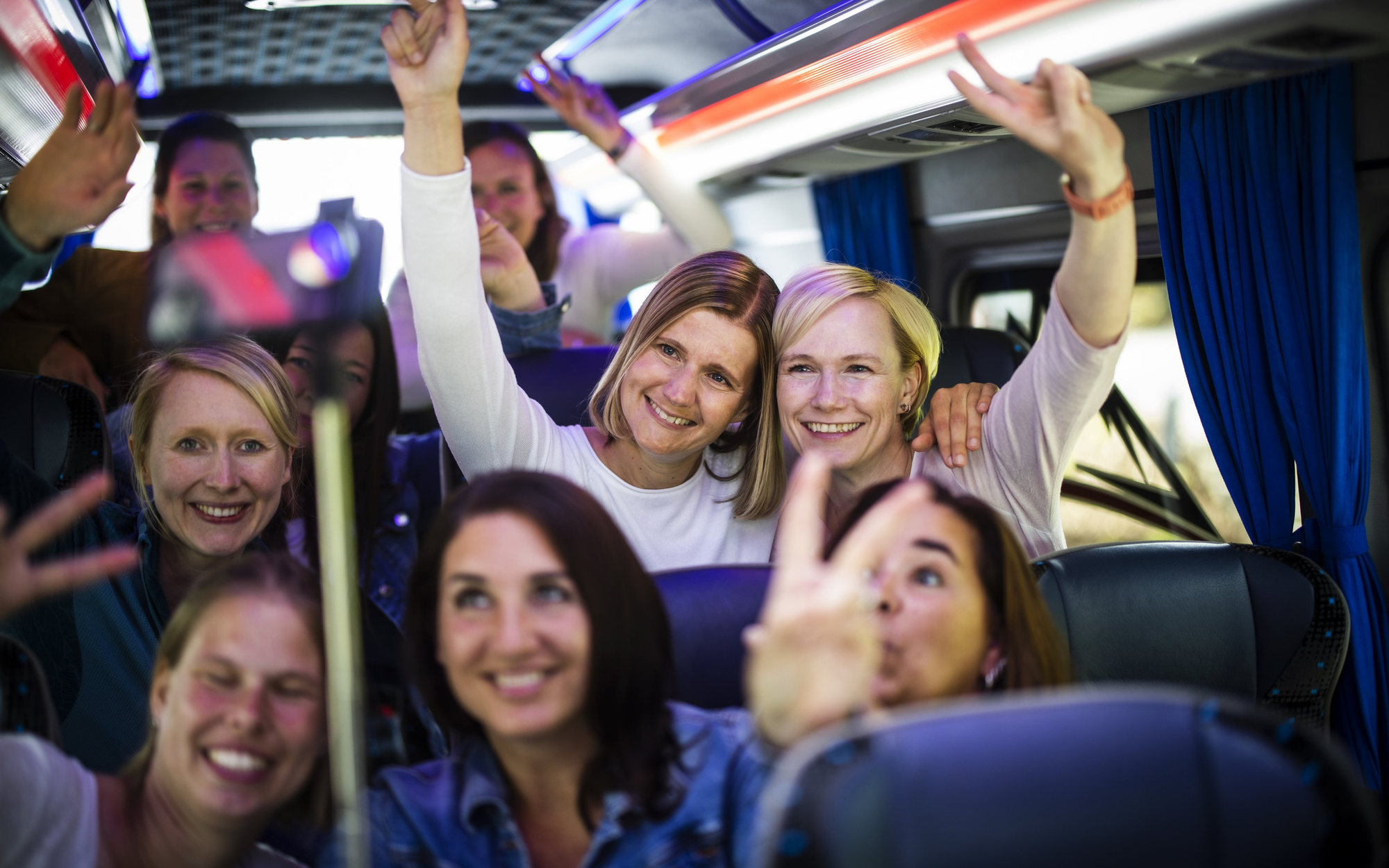 Mehrere Frauen, die im Bus sitzen und lächelnd mit den Fingern das Peace-Zeichen in Richtung kamera machen.