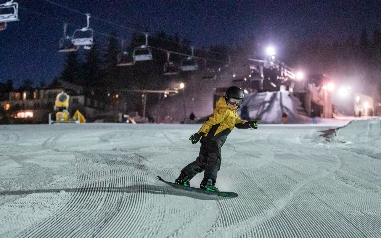 Ein Kind beim Snowboarden unter Flutlicht auf der Postwiese