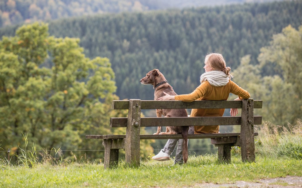Eine Frau macht zusammen mit ihrem Hund Pause auf einer Bank.