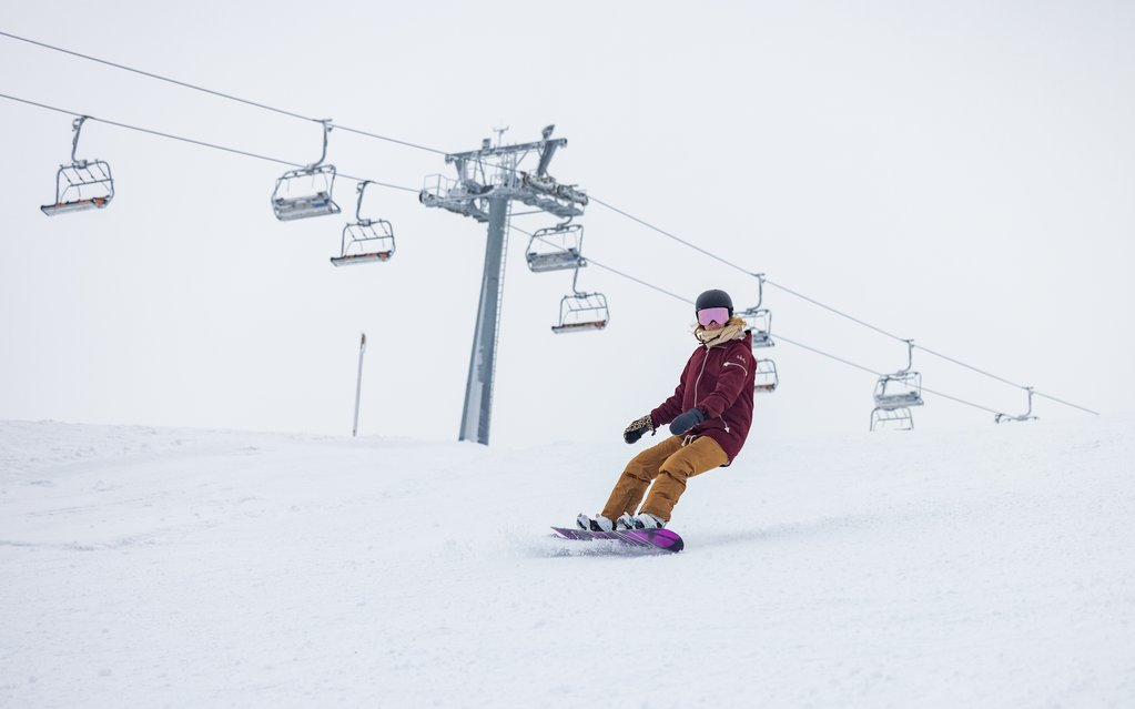 Ein Snowboardfahrer fährt auf seinem Snowboard einen Skihang hinunter.