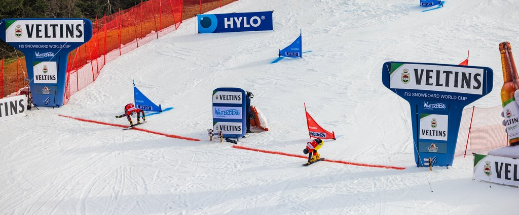 Zwei Snowboardfahrer überqueren nach einem Wettrennen die Ziellinie.