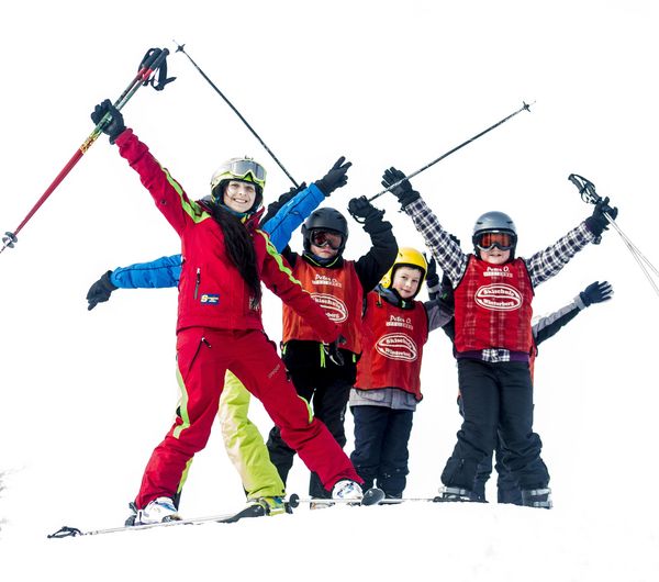 Mehrere Kinder jubeln mit ihrer Skilehrerin auf einer Piste