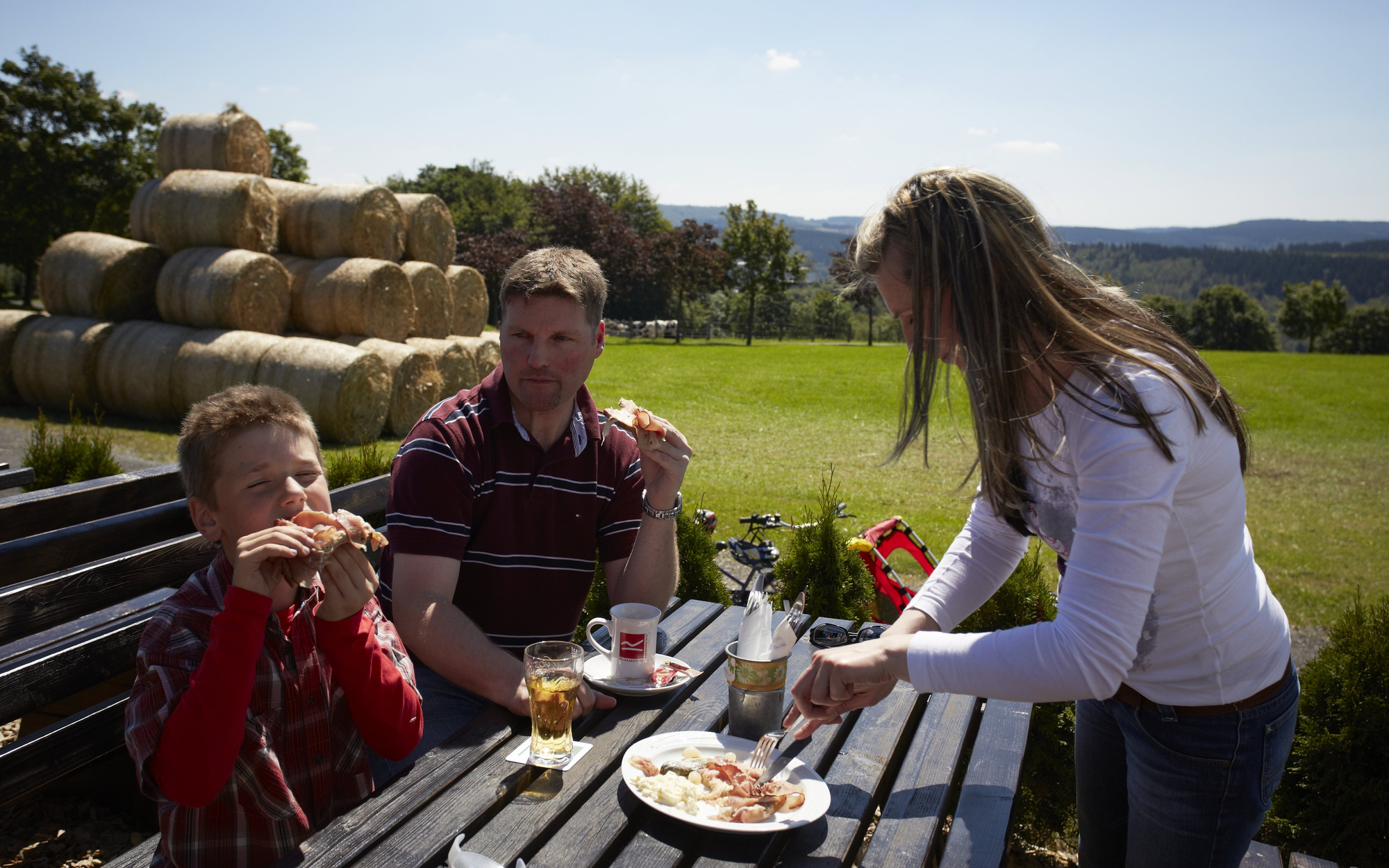 Eine Familie beim Picknick auf einer Bank mit Tisch in der Natur.