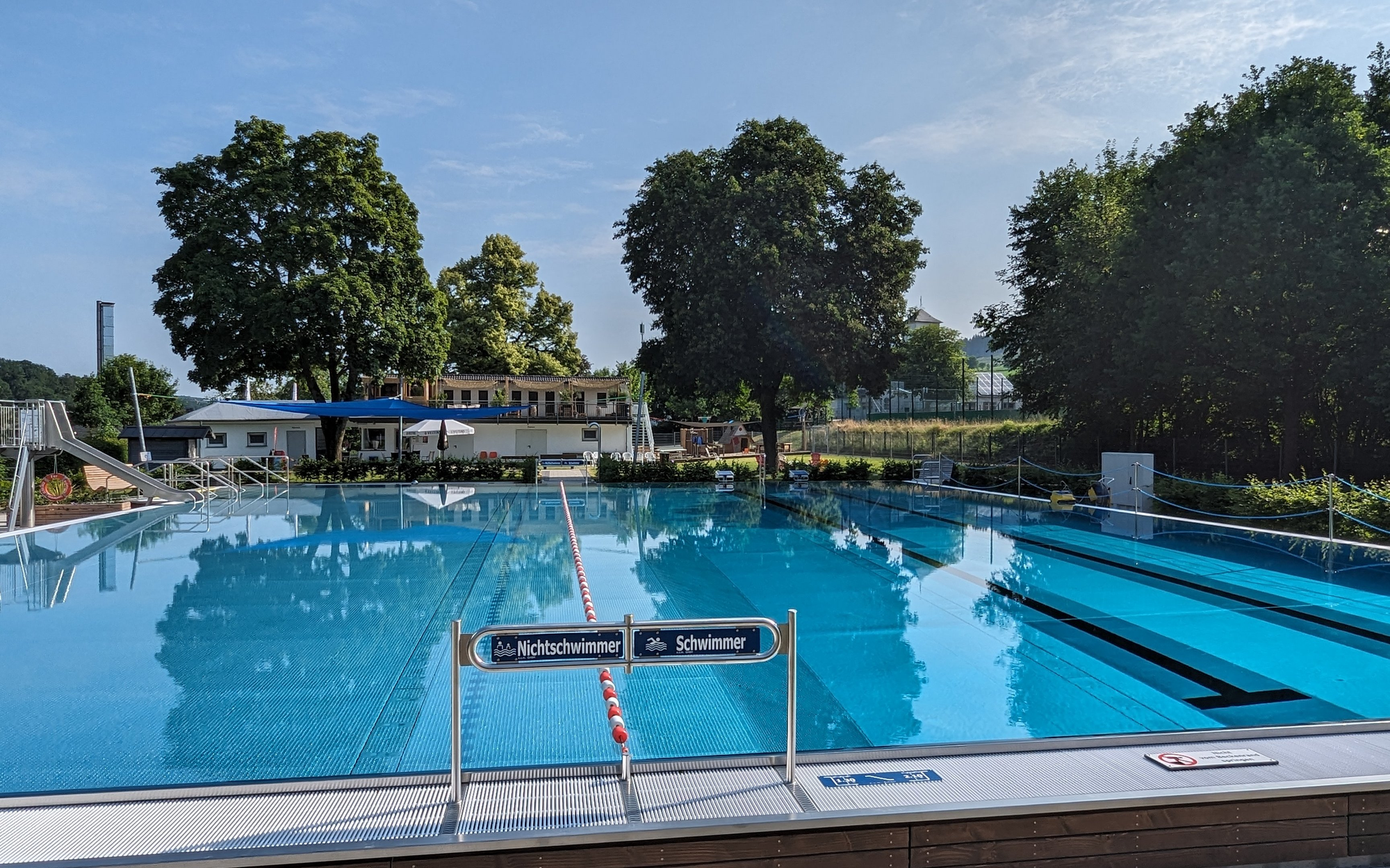 Freibad mit Rutsche und Hinweisschild Schwimmer und Nichtschwimmer im Vordergrund.