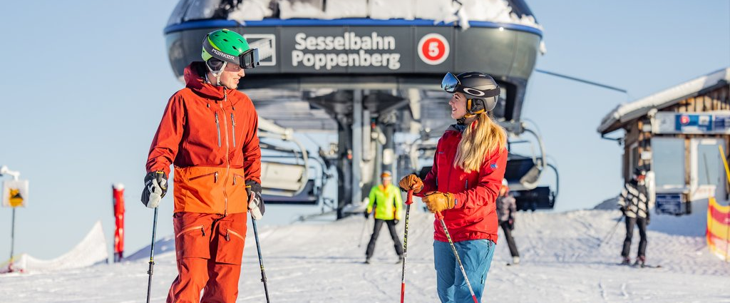 Zwei Skifahrer stehen vor dem Ausstieg eines Sesselliftes und schauen sich an.