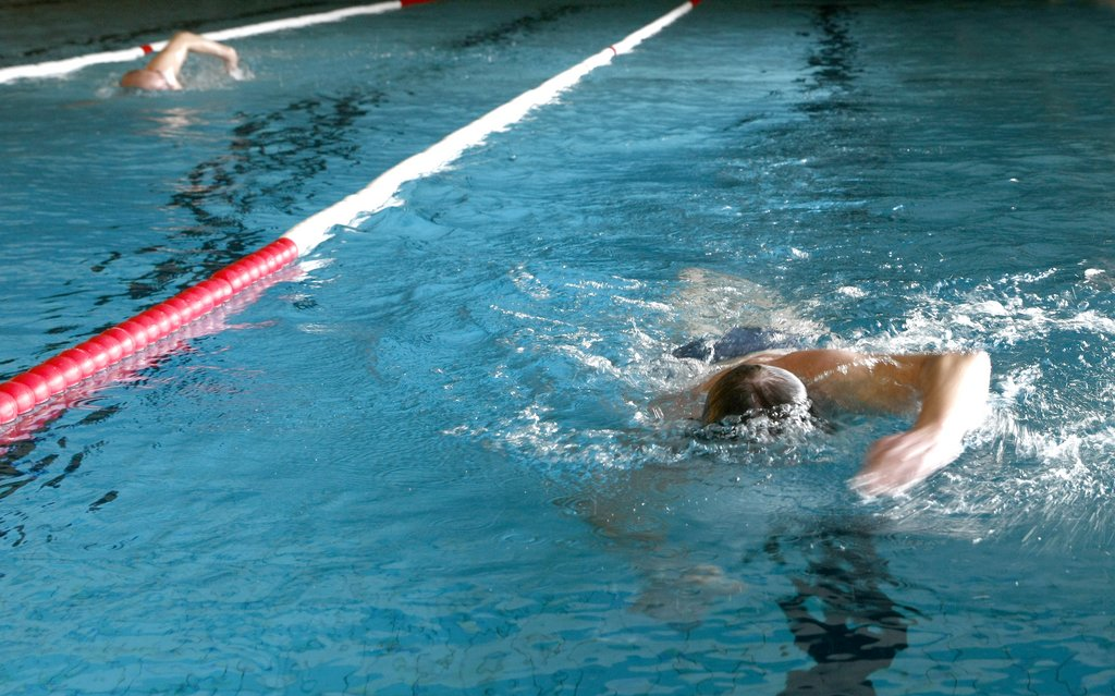 Zwei Personen, die im Kraulstil durch ein Sportbecken schwimmen.