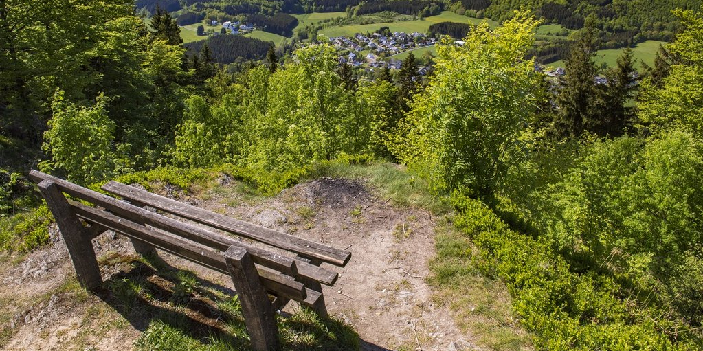 Man schaut über eine Bank und Wälder hinweg hinab ins Tal auf das Dorf Elkeringhausen.