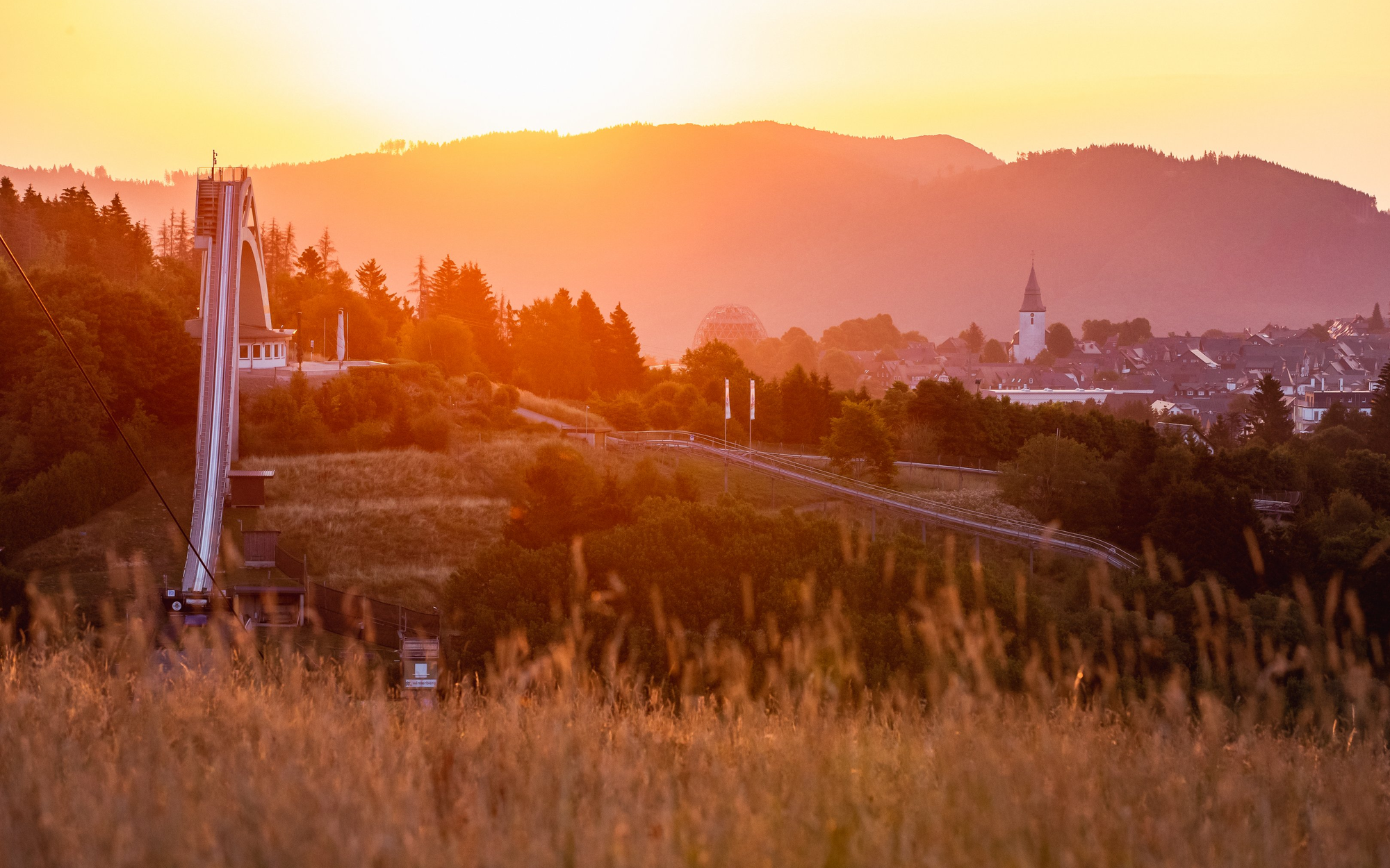 Die St. Georg Sprungschanze mit einem Teil der Stadt Winterberg und dem Kirchturm im Sonnenuntergang.