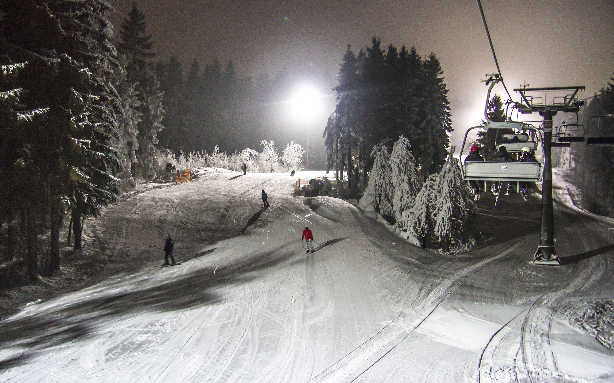 Ein paar Skifahrer fahren bei Flutlicht einen Skihang hinab.
