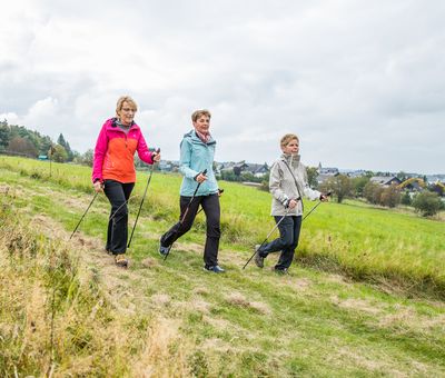 Drei Nordic Walkerinnen beim Abstieg auf einem Feldweg mit der Stadt Winterberg im Hintergrund