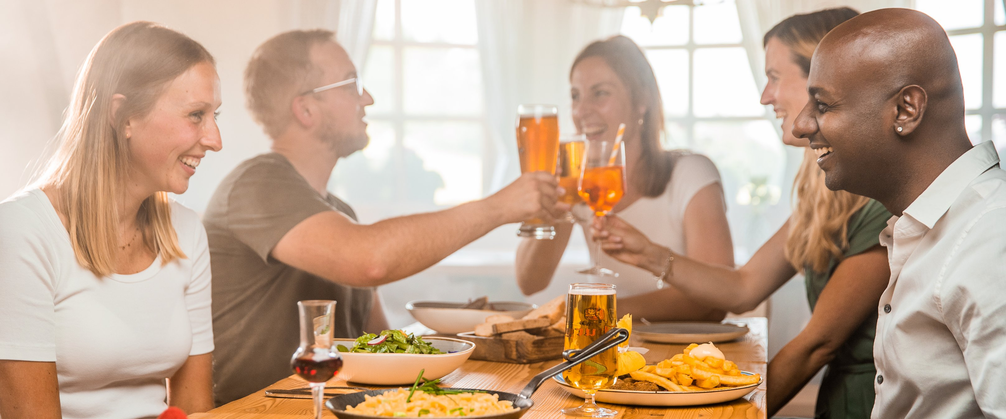 Gruppe von Freunden beim gemeinsamen Essen und Trinken in einer rustikalen Skihütte.