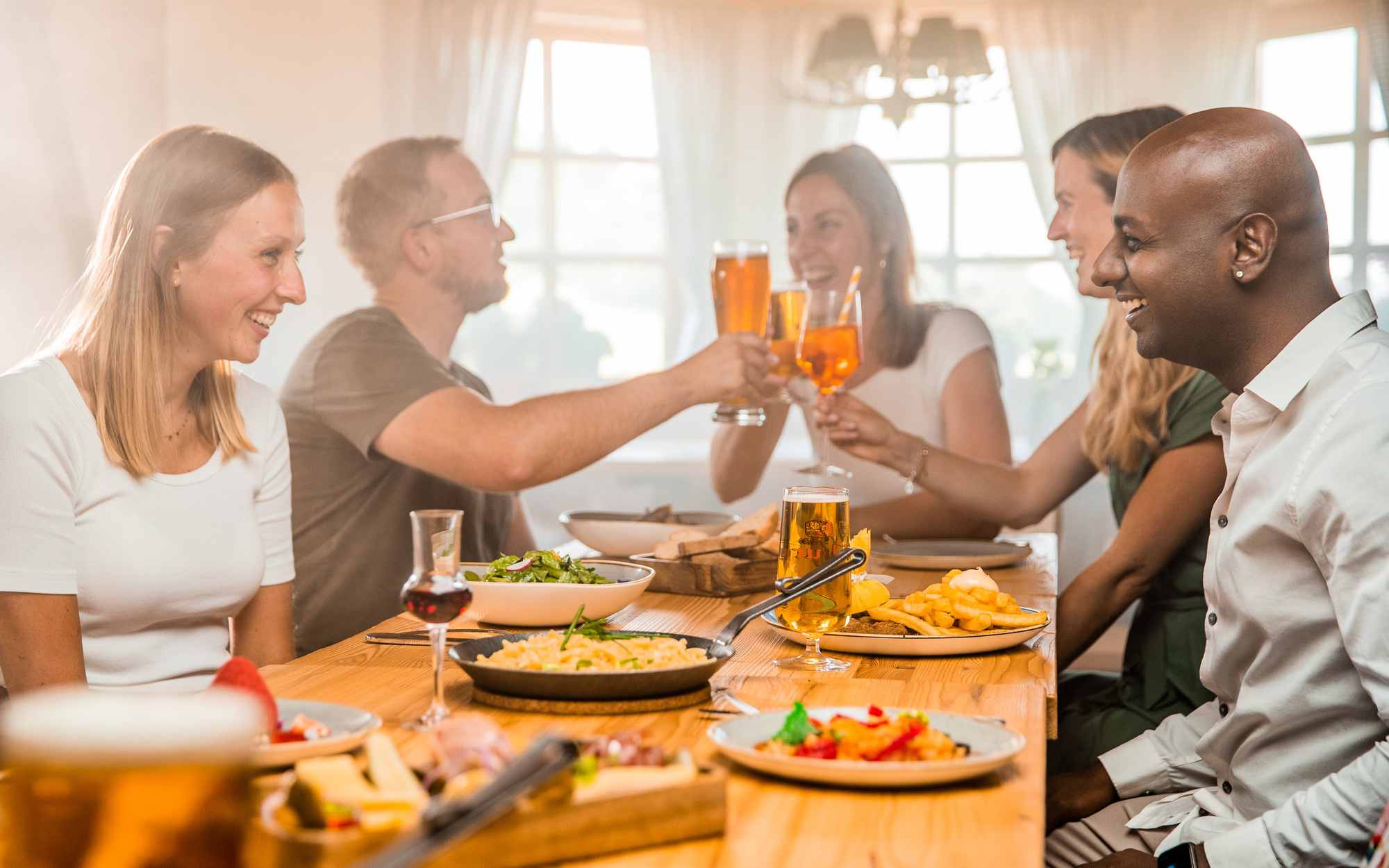 Gruppe von Freunden beim gemeinsamen Essen und Trinken in einer rustikalen Skihütte.
