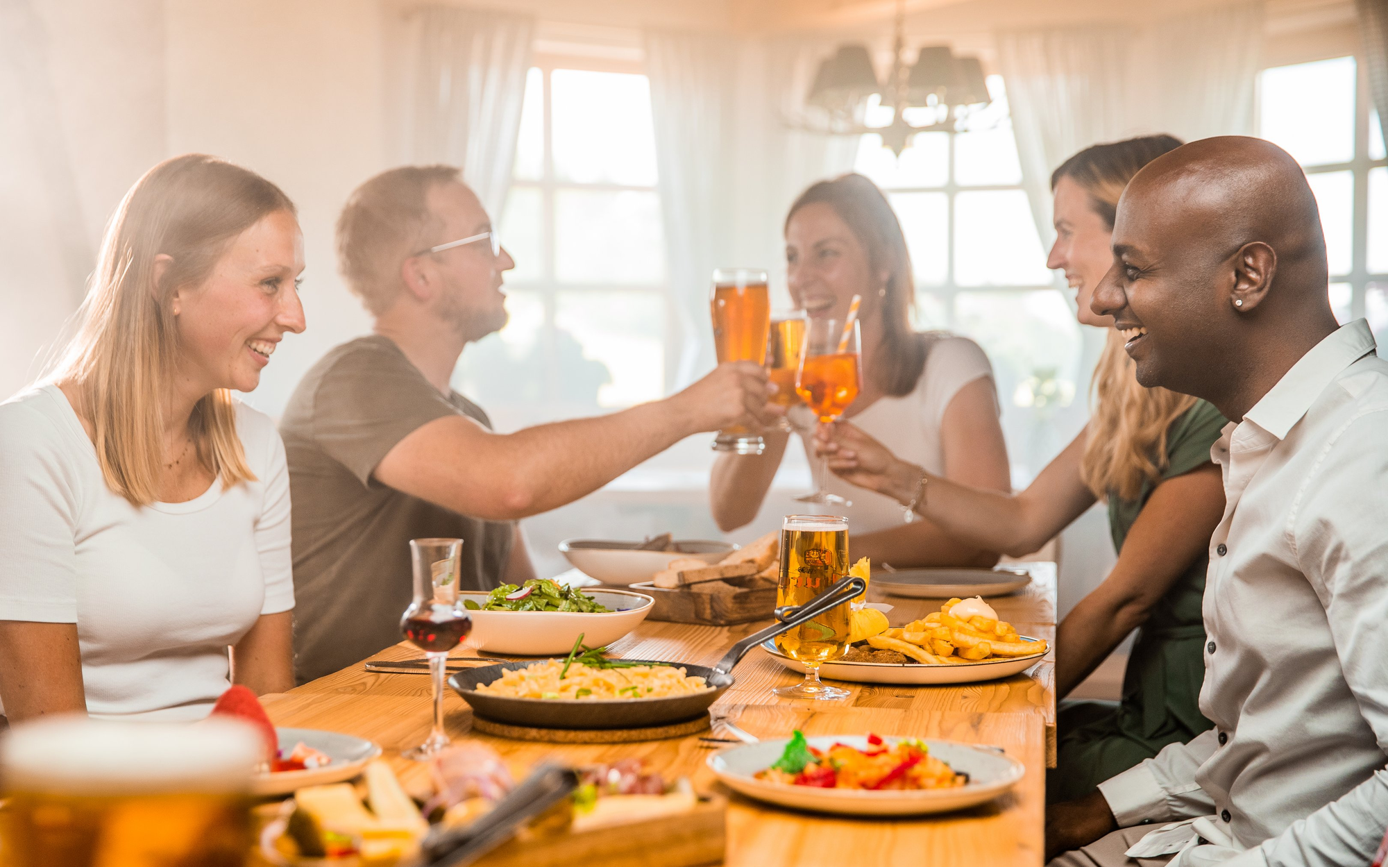 Gruppe von Freunden beim gemeinsamen Essen und Trinken in einer rustikalen Skihütte.