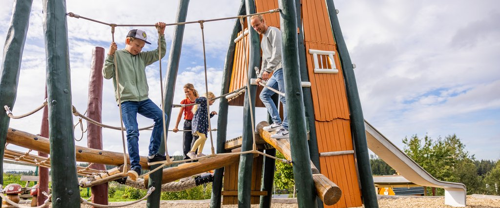 Familie mit zwei Kindern von denen eins über ein Seil balanciert.