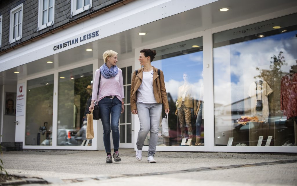 Zwei Frauen, die vor einem Schaufenster eines Geschäftes herlaufen.