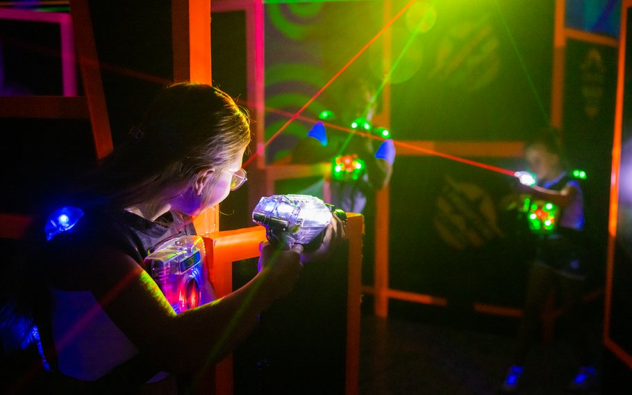 Zwei Frauen halten Laserpistolen in der Hand und versuchen sich gegenseitig im dunklen Raum mit den Lasern zu treffen.