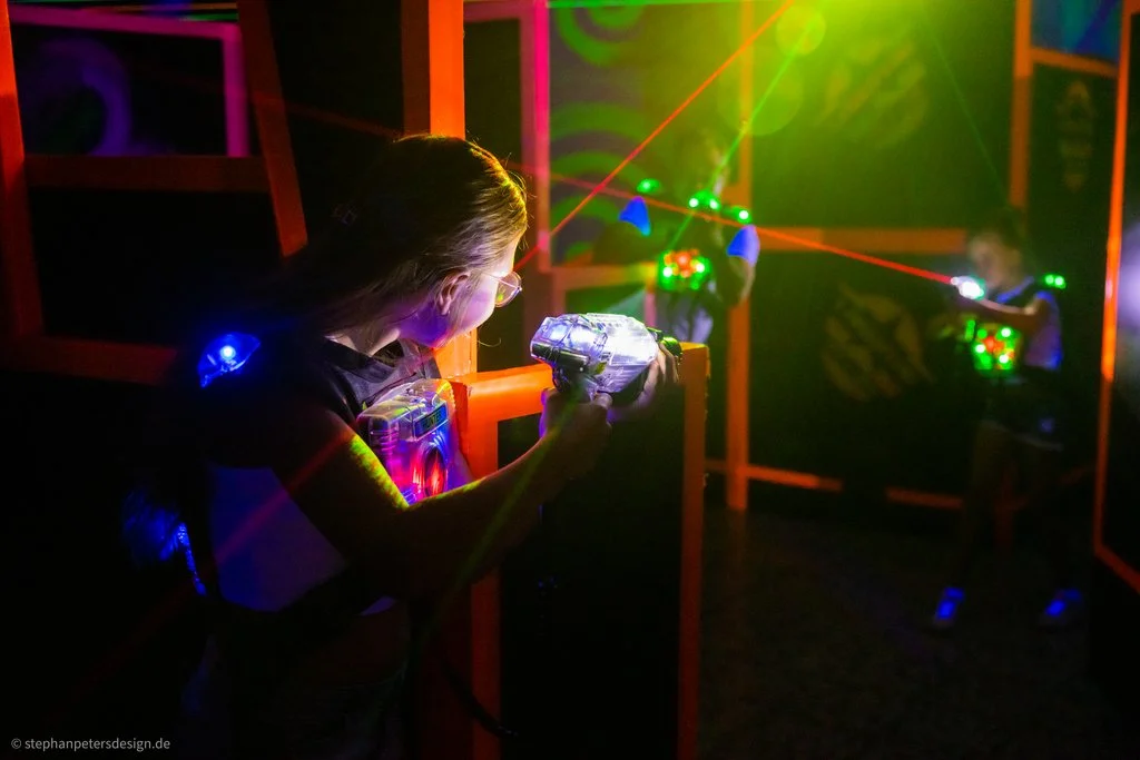 Zwei Frauen halten Laserpistolen in der Hand und versuchen sich gegenseitig im dunklen Raum mit den Lasern zu treffen.