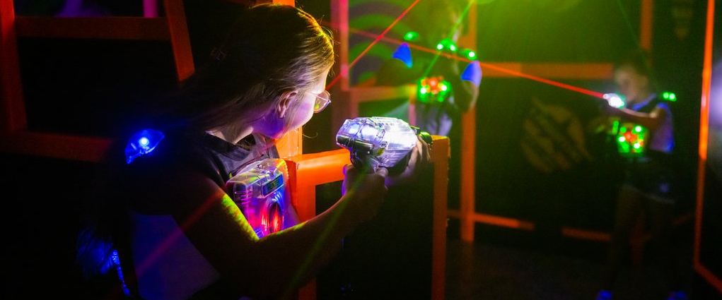 Zwei Frauen halten Laserpistolen in der Hand und versuchen sich gegenseitig im dunklen Raum mit den Lasern zu treffen.