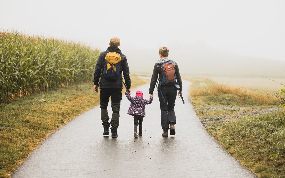 Ein Kind hält Mutter und Vater an den Händen und sie wandern einen Feldweg entlang.