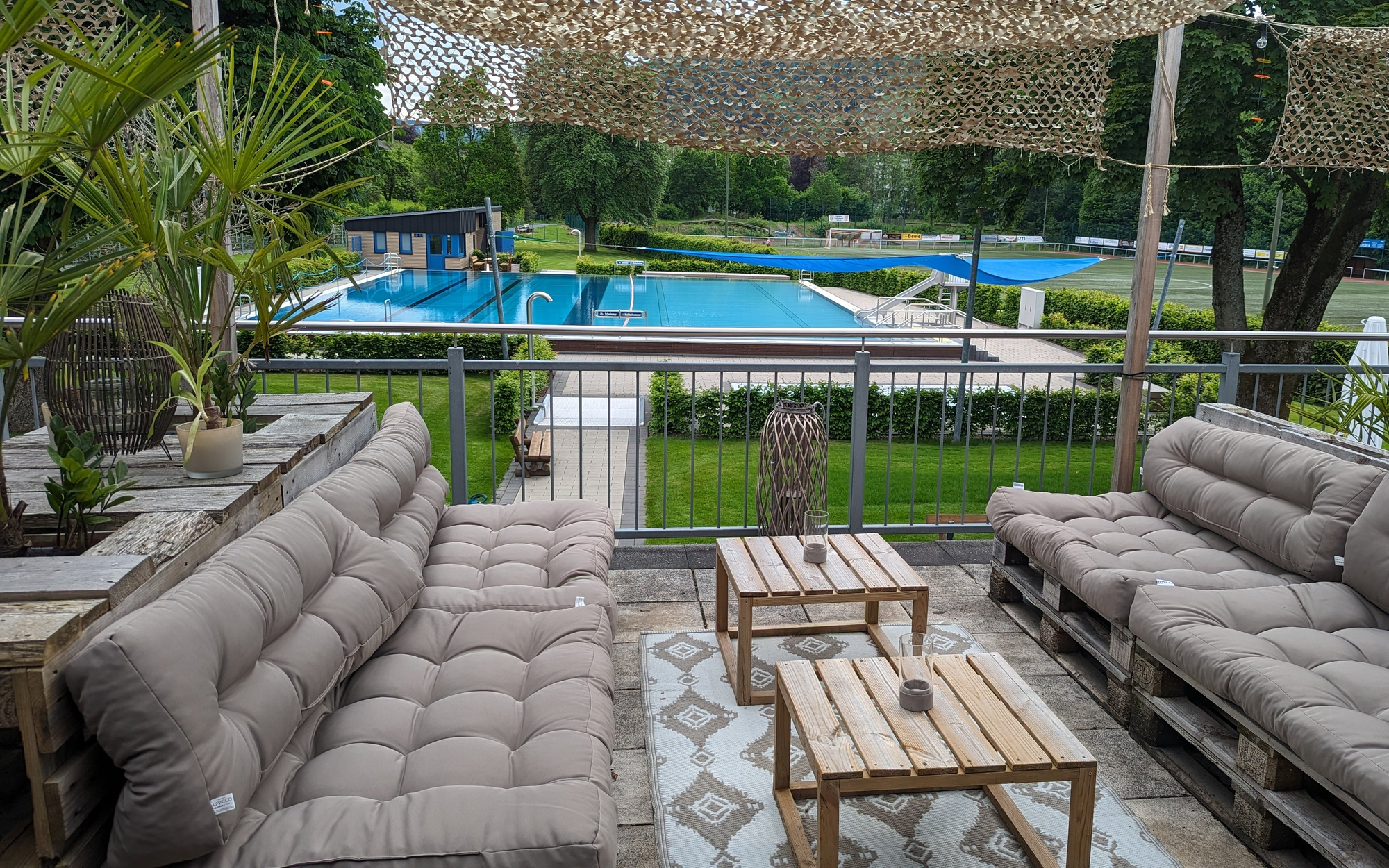Blick von der Terrasse mit gemütlichen Palettenmöbeln runter auf das Freibad.