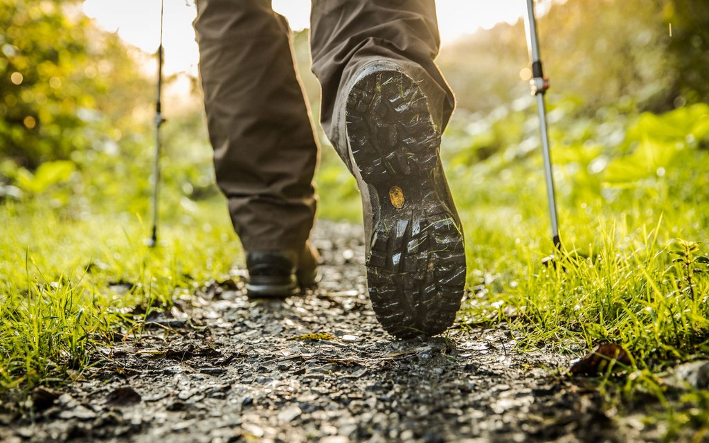 Ein paar Beine mit Wanderschuhen, die einen Waldweg entlang wandern.
