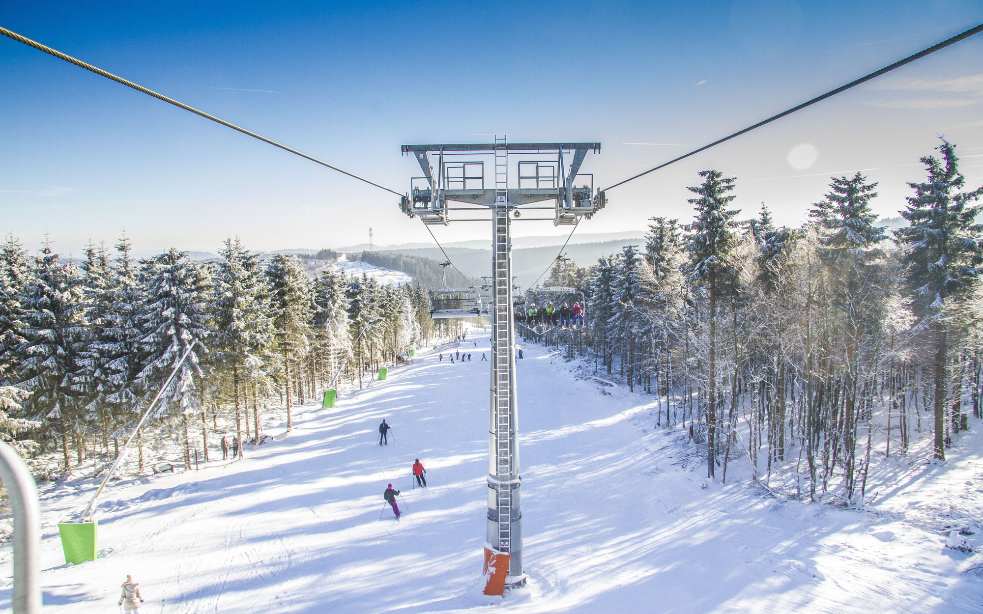 Ein Sessellift, der über einen Skihang mit Ski- und Snowboardfahrern hinwegfährt.