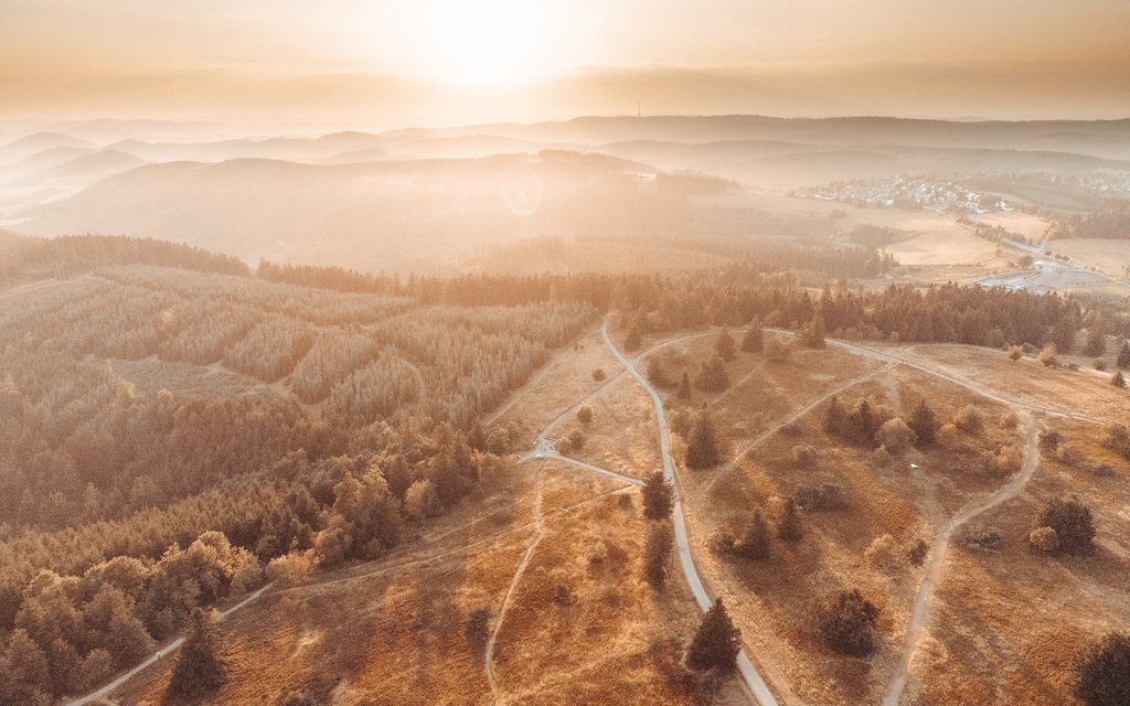 Eine Luftaufnahme einer herbtlichen Landschaft bei Sonnenaufgang im Nebel.