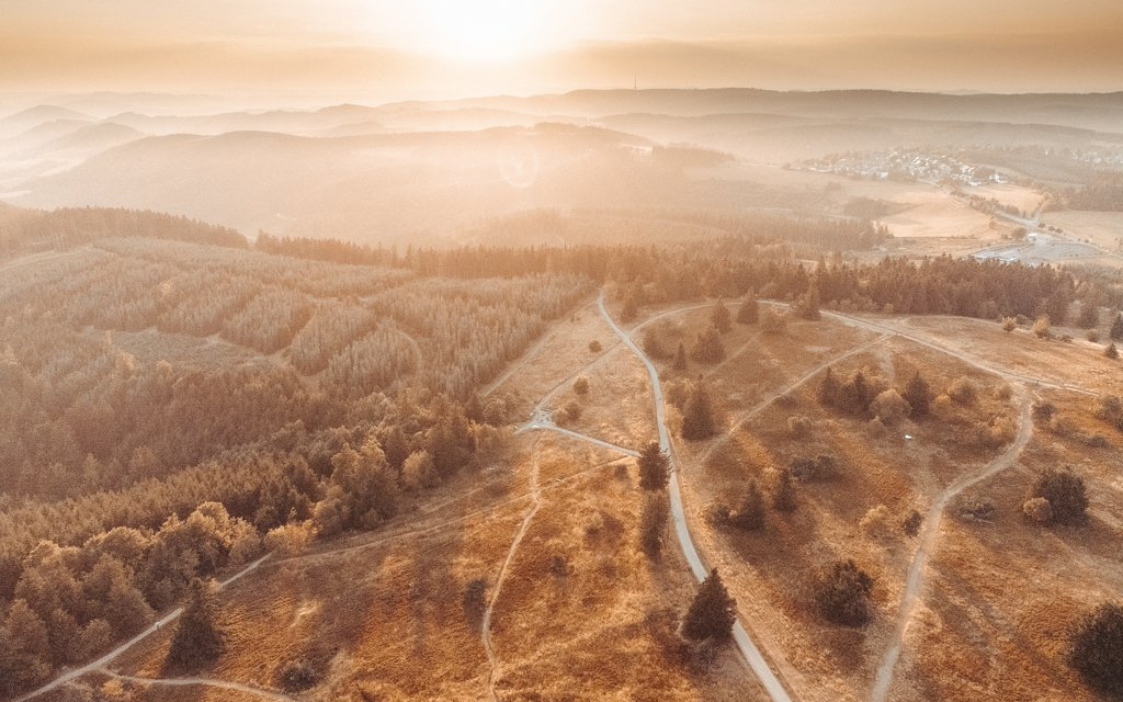 Eine Luftaufnahme einer herbtlichen Landschaft bei Sonnenaufgang im Nebel.