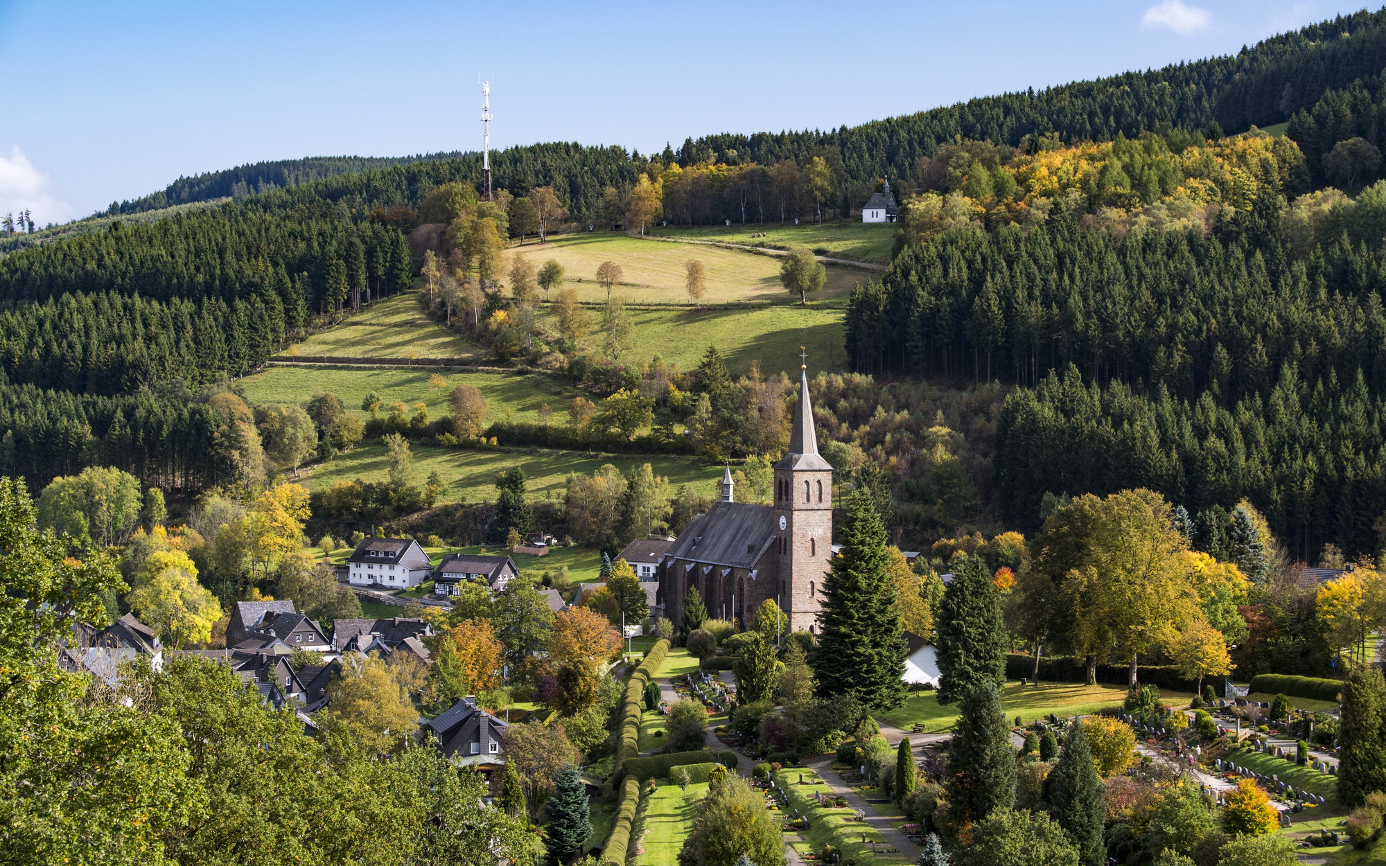 Blick auf die Ortschaft Züschen mit Kirchturm umgeben von Wäldern und Bergen.